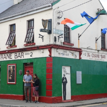 A cozy pub in Galway City with a traditional Irish exterior, colorful flower baskets, and inviting entrance, including a sign reading "Crane Bar."
