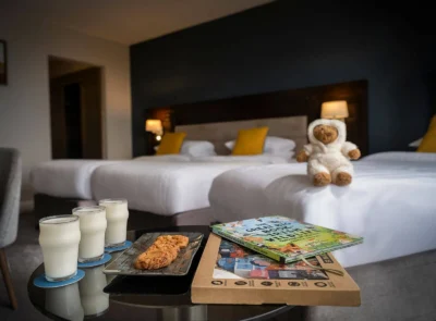 A cozy family hotel room with two double beds, modern decor, art on the walls, and a window offering natural light.