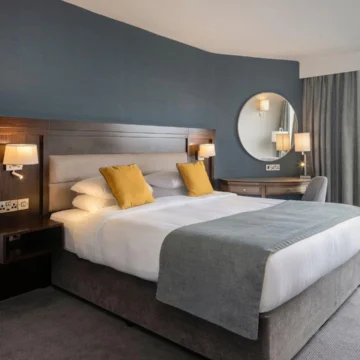 Elegant hotel room with two large beds, a cozy seating area, warm lighting, modern decor, and a connecting door to an adjacent room, offering a comfortable and spacious environment.