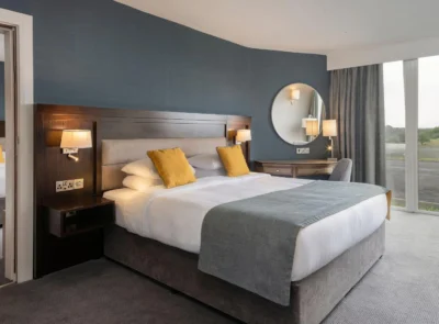 Elegant hotel room with two large beds, a cozy seating area, warm lighting, modern decor, and a connecting door to an adjacent room, offering a comfortable and spacious environment.