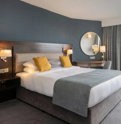 Elegant hotel room with two large beds, a cozy seating area, warm lighting, modern decor, and a connecting door to an adjacent room, offering a comfortable and spacious environment.