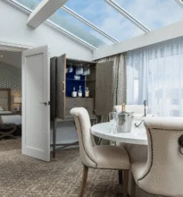 Luxurious hotel room featuring a large bed, elegant decor, comfortable seating area, ambient lighting, and a window offering a scenic view, creating a sophisticated and relaxing atmosphere.
