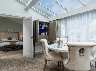 Luxurious hotel room featuring a large bed, elegant decor, comfortable seating area, ambient lighting, and a window offering a scenic view, creating a sophisticated and relaxing atmosphere.