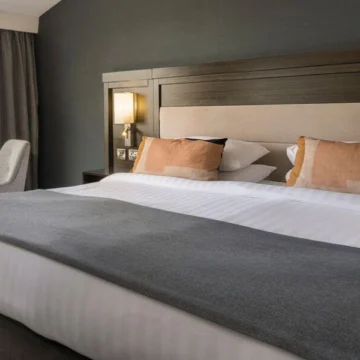 Luxurious hotel room featuring a large, comfortable bed with plush white bedding, elegant lighting fixtures, and a serene, inviting atmosphere for relaxation and comfort.