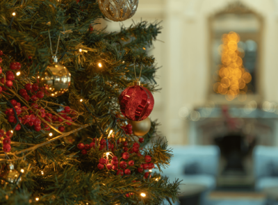 A cozy seaside hotel decorated with festive Christmas lights, featuring a snow-dusted landscape, a warmly lit building, and a peaceful ocean view in the background.