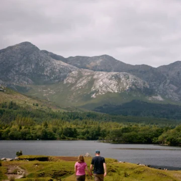 A scenic view of the Connemara Greenway, Co Galway, featuring a tranquil path surrounded by lush greenery and mountainous landscape under a clear blue sky.