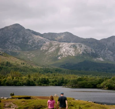 A scenic view of the Connemara Greenway, Co Galway, featuring a tranquil path surrounded by lush greenery and mountainous landscape under a clear blue sky.