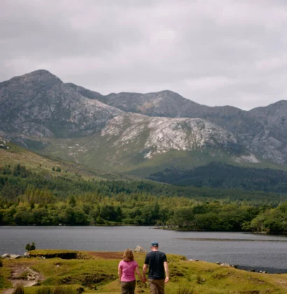 A scenic view of the Connemara Greenway, Co Galway, featuring a tranquil path surrounded by lush greenery and mountainous landscape under a clear blue sky.