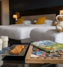 A spacious, well-lit family hotel room with a large bed, two smaller beds, elegant furnishings, a seating area, and windows offering a scenic view.