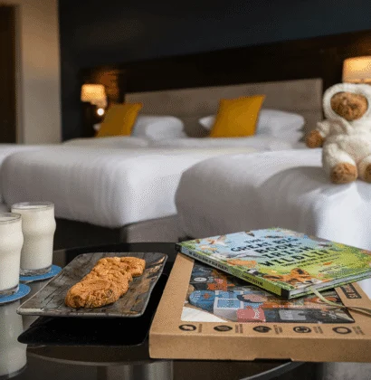 Family-friendly twin room with two plush beds, bedside lamps, teddy, milk, cookies and children’s books on a bedside table, cosy stay