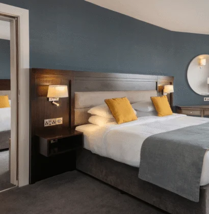 A hotel room with two beds, stylish decor, carpeted floor, bedside lamps, and large windows offering a scenic view over a body of water.