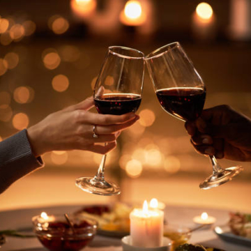 Glasses of red wine coming together over candle light