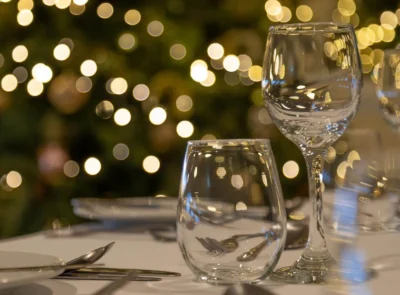 Festively decorated interior with Christmas trees, tables set for dining, chairs, and twinkling lights, creating a warm, inviting atmosphere suitable for a holiday gathering or party.
