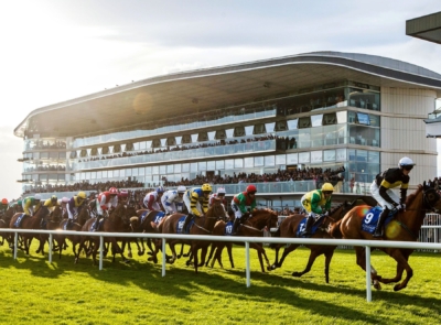 Image of a coastal hotel nestled by a serene blue sea, surrounded by lush greenery and hills, under a bright, clear sky.