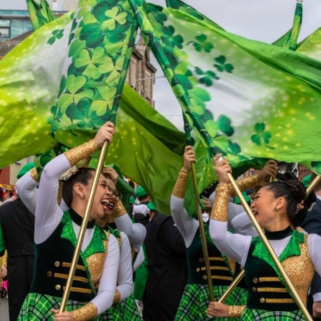 A cozy hotel room featuring a large bed with plush pillows and blanket, nightstands with lamps, and a scenic view of the sea through the window.