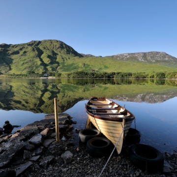 A luxurious hotel room with a neatly made double bed, pillows, wooden furniture, stylish lamp, and ocean-view windows creating a serene, inviting atmosphere for relaxation.
