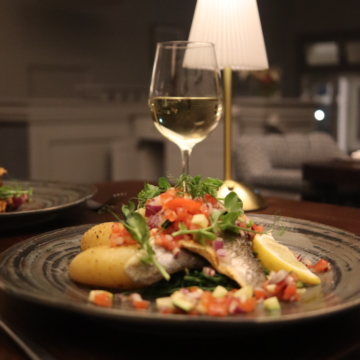 Coastal view from Connemara Coast Hotel: rocky shoreline with seaweed-covered rocks, gentle sea waves, cloudy sky, and rolling hills in the distance. Serene and picturesque scenery.