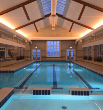 Guests enjoying serene indoor pool with skylight, warm lighting, and sea views. Relaxing swim experience at seaside hotel.
