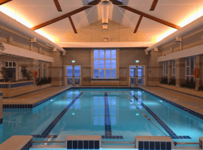 Guests enjoying serene indoor pool with skylight, warm lighting, and sea views. Relaxing swim experience at seaside hotel.