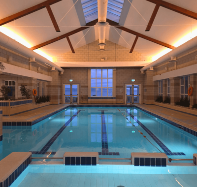 Guests enjoying serene indoor pool with skylight, warm lighting, and sea views. Relaxing swim experience at seaside hotel.