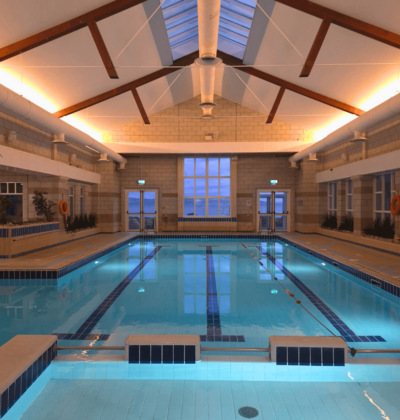 Guests enjoying serene indoor pool with skylight, warm lighting, and sea views. Relaxing swim experience at seaside hotel.