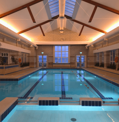 Guests enjoying serene indoor pool with skylight, warm lighting, and sea views. Relaxing swim experience at seaside hotel.