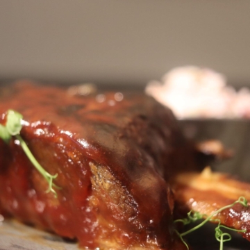 Juicy beef short rib on a plate, served with a rich sauce reduction, garnished with fresh herbs and colorful vegetables, creating an appetizing and elegant presentation.