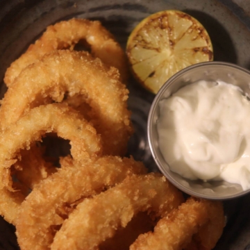 A plate of deep-fried calamari rings garnished with fresh parsley, served with a small bowl of dipping sauce on the side.