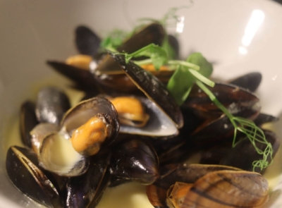 A plate of steamed mussels garnished with fresh herbs and lemon wedges, presented beautifully for fine dining.