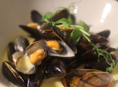A plate of cooked mussels served in their shells, garnished with herbs and lemon slices, positioned on an elegant white tablecloth.