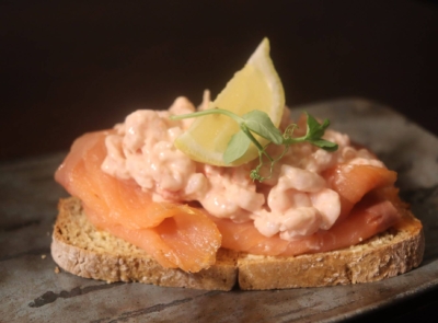 A delicious dish featuring smoked salmon and prawns, garnished with greens and lemon slices, elegantly presented on a white plate atop a rustic wooden surface.