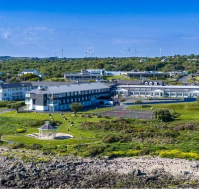 Back view of Connemara Coast Hotel with lush green lawns, outdoor seating, and partly cloudy sky.