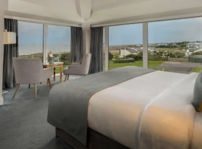 Elegant hotel room with a king-sized bed, ocean-view balcony, plush seating area, soft warm lighting, decorated in soothing neutral tones, evoking relaxation and luxury by the coast.