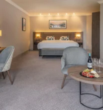 Coastal suite room with a large bed, modern decor, window with ocean view, and elegant furnishings in neutral tones.