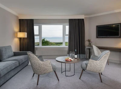A cozy suite with a large bed, elegant furnishings, a seating area, and a stunning ocean view through a wide window, exuding a serene and luxurious atmosphere.