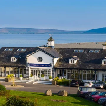 A scenic coastal hotel view with grassy foreground, overlooking a calm sea, under a partially cloudy sky, reflecting tranquility and natural beauty.