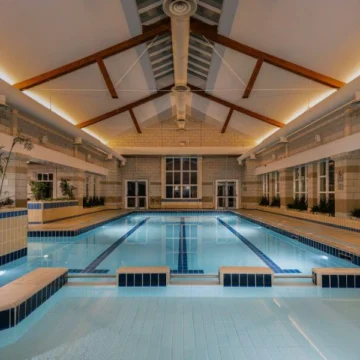 A luxurious indoor pool with clear blue water, surrounded by elegant floral decorations and large windows offering an inviting and serene aquatic experience.