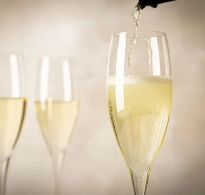 A hand pouring prosecco into a flute glass, with gentle bubbles rising within the glass, set against a softly focused background.