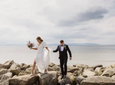 A beautifully set wedding reception area with elegant table arrangements, floral centerpieces, white chairs, and a scenic backdrop of the ocean and clear blue skies.