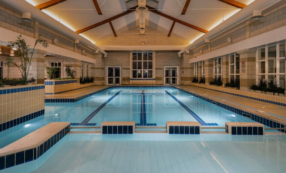 Indoor heated hotel swimming pool with lane markings, tiled benches, plant planters and vaulted wood-beam ceiling, ideal for leisure or fitness
