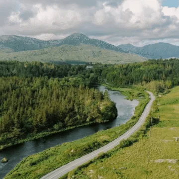 A scenic landscape photo of Connemara National Park featuring lush green hills, a serene lake, blue skies, and a mountainous backdrop.