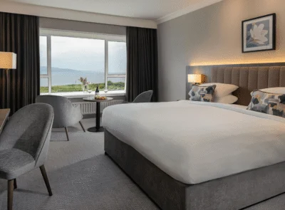 Ocean view from a hotel room with a comfortable king-sized bed, plush sofa, and large windows offering a stunning seaside landscape and natural light.