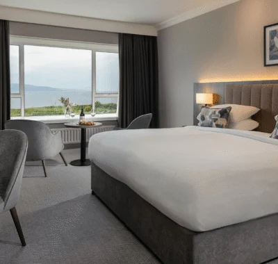 Ocean view from a hotel room with a comfortable king-sized bed, plush sofa, and large windows offering a stunning seaside landscape and natural light.