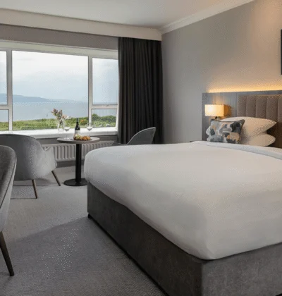 Ocean view from a hotel room with a comfortable king-sized bed, plush sofa, and large windows offering a stunning seaside landscape and natural light.