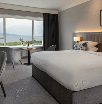 Ocean view from a hotel room with a comfortable king-sized bed, plush sofa, and large windows offering a stunning seaside landscape and natural light.