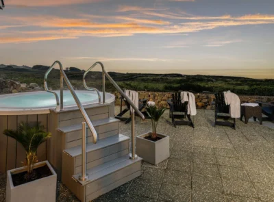 Outdoor hot tub overlooking a serene lake during dusk, surrounded by handrails and a wooden deck, under a vibrant sunset sky with scattered clouds.